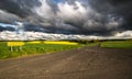 Empty road in the countryside, large dark clouds, sunset light.