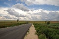Empty road and field with beautiful fluffy clouds in the sky. Royalty Free Stock Photo