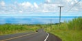 Empty road in Hawaiian countryside with car and ocean in background Royalty Free Stock Photo