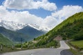 Empty road serpentine in the mountains, blue sky with clouds, mountain peaks in the snow and green hills background Royalty Free Stock Photo