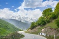 Empty road serpentine in the mountains, blue sky with clouds, mountain peaks in the snow and green hills background Royalty Free Stock Photo