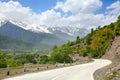 Empty road serpentine in the mountains, blue skywith clouds, mountain peaks in the snow and green hills background Royalty Free Stock Photo