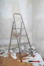 Empty room with bare walls ladder and old wallpaper scraps on floor during redecoration