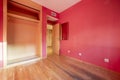 Empty room with deteriorated wooden floor with red walls and cupboard without doors