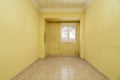 Empty room with light stoneware floor, dirty yellow painted walls, aluminum window with views and plaster border on the ceilings