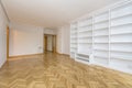 empty room with a wall covered with a white painted masonry bookcase, varnished and polished French oak parquet floors laid in a