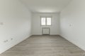 Empty room with white painted walls, white wooden skirting boards, white aluminum windows, white aluminum radiator inside a niche
