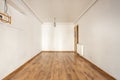 Empty room with a wooden floor, plaster moldings on the ceiling, an aluminum radiator, a gray ceiling lamp and matching skirting