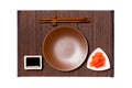 Empty round brown plate with chopsticks for sushi, ginger and soy sauce on dark bamboo mat background. Top view with copy space Royalty Free Stock Photo