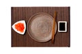 Empty round brown plate with chopsticks for sushi, ginger and soy sauce on dark bamboo mat background. Top view with copy space Royalty Free Stock Photo
