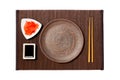 Empty round brown plate with chopsticks for sushi, ginger and soy sauce on dark bamboo mat background. Top view with copy space Royalty Free Stock Photo