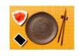 Empty round brown plate with chopsticks for sushi, ginger and soy sauce on yellow bamboo mat background. Top view with copy space Royalty Free Stock Photo