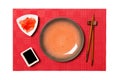 Empty round brown plate with chopsticks for sushi and soy sauce, ginger on red mat sushi background. Top view with copy space for Royalty Free Stock Photo