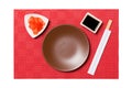 Empty round brown plate with chopsticks for sushi and soy sauce, ginger on red mat sushi background. Top view with copy space for Royalty Free Stock Photo