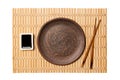 Empty round brown plate with chopsticks for sushi and soy sauce on yellow bamboo mat background. Top view with copy space for you Royalty Free Stock Photo