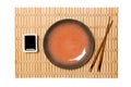 Empty round brown plate with chopsticks for sushi and soy sauce on yellow bamboo mat background. Top view with copy space for you Royalty Free Stock Photo