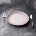 An empty round ceramic plate, knife, and fork as a dining table setting. An empty plate Royalty Free Stock Photo