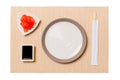 Empty round white plate with chopsticks for sushi, ginger and soy sauce on brown sushi mat background. Top view with copy space Royalty Free Stock Photo