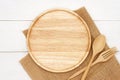 Empty round wooden plate with spoon, fork and rustic brown burlap cloth on white wooden table. Royalty Free Stock Photo