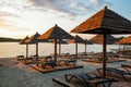 Empty rows resting places on evening sandy beach with brown wooden loungers and umbrellas Royalty Free Stock Photo