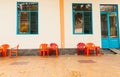 Empty sets of red and orange chairs and tables on footpath out side building with blue door and windows Royalty Free Stock Photo