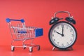 An empty shopping cart and an alarm clock on a red scarlet background Royalty Free Stock Photo
