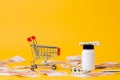 An empty shopping cart and a jar of pills. Yellow background with scattered money. Copy space. The concept of the high cost of Royalty Free Stock Photo