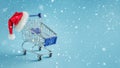 Empty shopping trolley and santa hat on blue snowy background