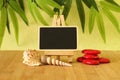 empty slate in width to write a message posed on an easel on a wooden floor with red pebble and beach shells on a green foli