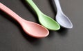 Empty spoons in different colours over black. Pink, green and purple spoon.