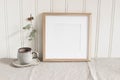 Empty square wooden picture frame mockup. Cup of coffee on linen table cloth. Dry eucalyptus taped on white wooden wall Royalty Free Stock Photo