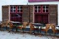 Empty street cafe in european old town. Empty tables and chairs against old white brick building with open shutters and red window Royalty Free Stock Photo