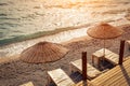 Empty sun bed chairs with matress and straw beach umbrellas on beach during sunset in summer Royalty Free Stock Photo