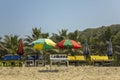 Empty sun loungers under the multi-colored beach umbrellas on the yellow sand against the green palm trees under a clear blue sky Royalty Free Stock Photo