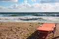 Empty sunbed by the sea, with waves splashing the beach sand in distance.