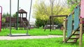 Empty swing with chains swaying at playground for child, moved from wind, on green meadow background in slow motion loopable