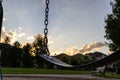 Empty swing at sunset - silhouetted against a backdrop of golden clouds and suburban homes Royalty Free Stock Photo