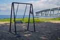 Empty swing swayed by the wind in shade of trees on the coastline seashore near of a big rounded Controlled-access motorway Royalty Free Stock Photo