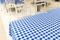 Empty table covered with blue and white chequered tablecloth next to white wooden chairs. Royalty Free Stock Photo