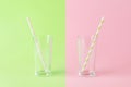 Empty tall glass with a pink paper drinking straw on a green background and one more with a green paper drinking straw on a pink