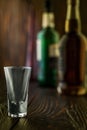 An empty tequila glass in front of many colorful liquor bottles, shallow depth of field, selective focus.