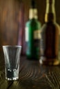 An empty tequila glass in front of many colorful liquor bottles, shallow depth of field, selective focus.