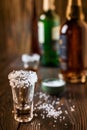 An empty tequila glass, with salt at the edges, stands on the bar, in the background are different bottles of alcohol