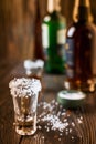 An empty tequila glass, with salt at the edges, stands on the bar, in the background are different bottles of alcohol