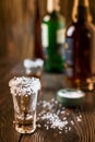 An empty tequila glass, with salt at the edges, stands on the bar, in the background are different bottles of alcohol