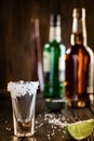 An empty tequila glass, with salt at the edges, stands on the bar, in the background are different bottles of alcohol