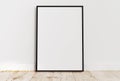 Empty thin black frame on light wooden floor with white wall behind it Royalty Free Stock Photo