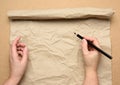 Empty torn sheet of brown craft paper and two hands with a black wooden pencil Royalty Free Stock Photo