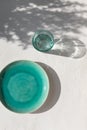 Empty turquoise ceramic plate with glass of water on white plaster background with leaves shadows. Spring or summer table setting. Royalty Free Stock Photo