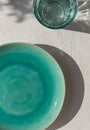 Empty turquoise ceramic plate with glass of water on white plaster background with leaves shadows. Royalty Free Stock Photo
